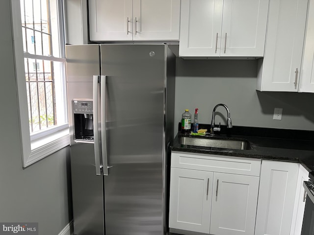 kitchen with dark stone counters, stainless steel refrigerator with ice dispenser, a sink, and white cabinetry