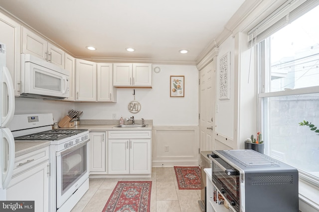 kitchen featuring a wainscoted wall, light countertops, light tile patterned floors, white appliances, and a sink