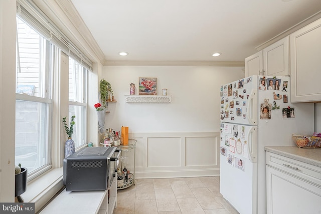 kitchen with ornamental molding, freestanding refrigerator, wainscoting, a decorative wall, and light tile patterned floors