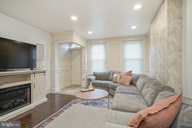 living room featuring a decorative wall, recessed lighting, ornate columns, and dark wood-style flooring