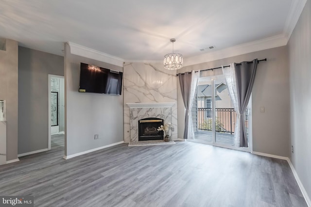 unfurnished living room featuring a chandelier, a premium fireplace, wood finished floors, visible vents, and baseboards