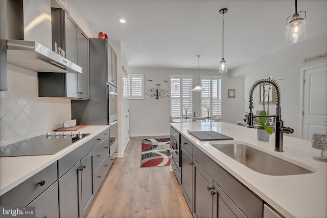 kitchen featuring wall chimney range hood, black electric stovetop, gray cabinets, and a sink