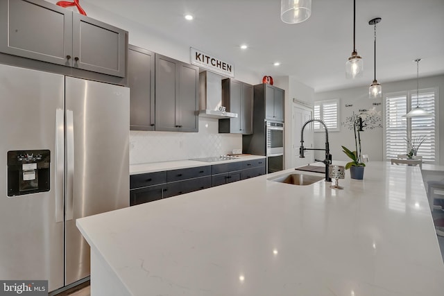 kitchen featuring stainless steel appliances, a sink, wall chimney exhaust hood, tasteful backsplash, and pendant lighting