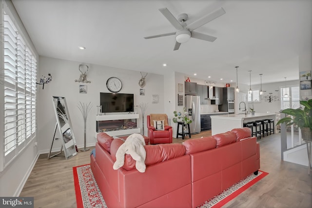 living area with baseboards, ceiling fan, light wood-type flooring, and recessed lighting