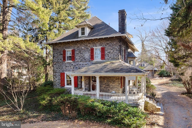 view of front facade with stone siding, a porch, a chimney, and a high end roof