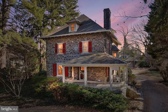 view of front of property with stone siding, a high end roof, covered porch, and a chimney