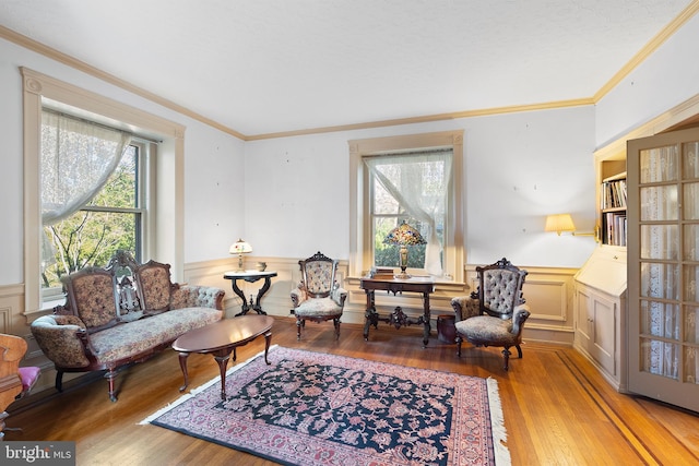 living area featuring a wainscoted wall, hardwood / wood-style floors, and crown molding