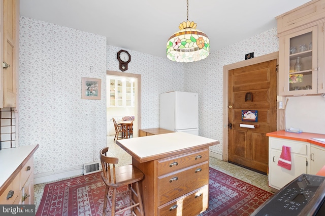 kitchen with visible vents, light countertops, freestanding refrigerator, glass insert cabinets, and wallpapered walls