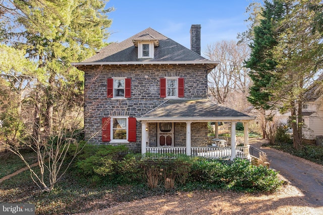 view of front of house with a porch, a high end roof, stone siding, and a chimney