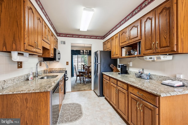 kitchen with light stone countertops, visible vents, a sink, appliances with stainless steel finishes, and brown cabinets