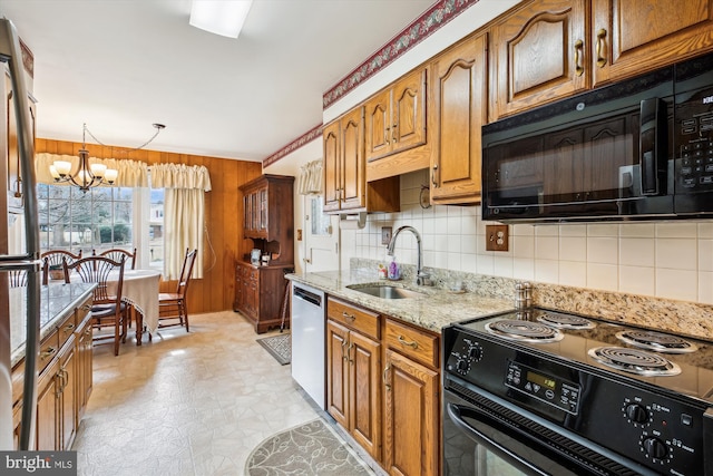 kitchen featuring brown cabinetry, wood walls, black appliances, and a sink