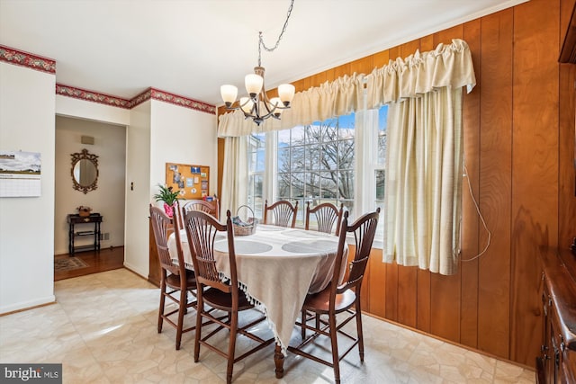 dining room featuring wood walls, baseboards, and an inviting chandelier