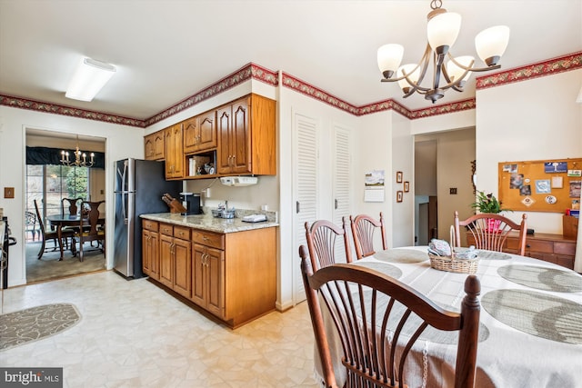 kitchen with light stone counters, freestanding refrigerator, an inviting chandelier, brown cabinetry, and hanging light fixtures