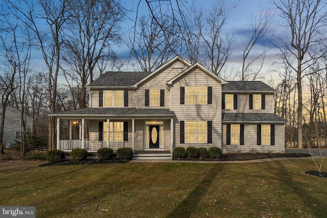 view of front of house with a shingled roof, covered porch, and a lawn