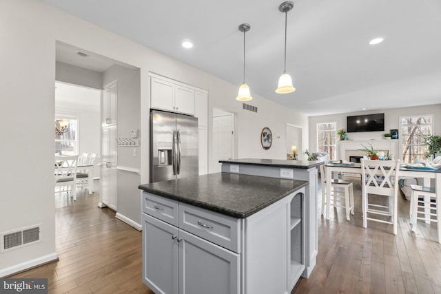 kitchen with dark countertops, stainless steel refrigerator with ice dispenser, visible vents, and a center island