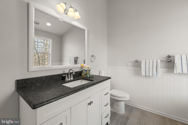 bathroom featuring visible vents, toilet, wainscoting, vanity, and wood finished floors