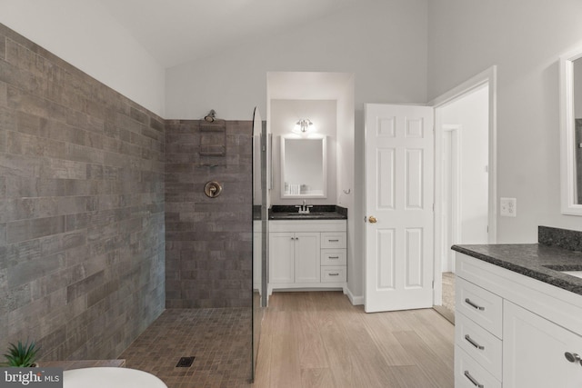 bathroom featuring a walk in shower, wood finished floors, two vanities, a sink, and vaulted ceiling