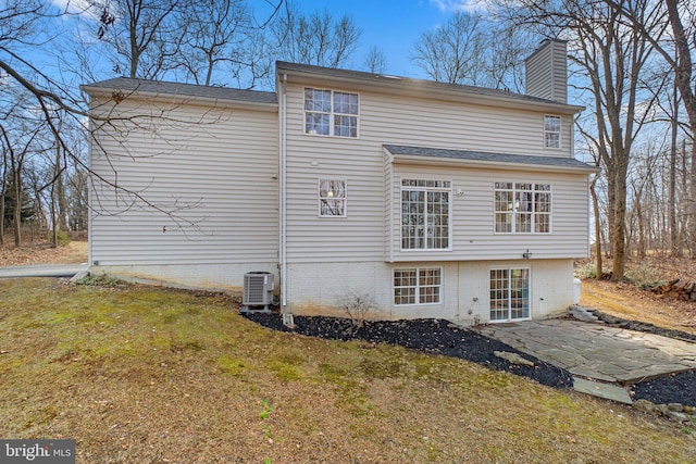 rear view of property featuring central air condition unit, a chimney, a lawn, and a patio