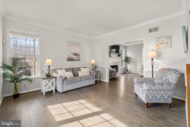 living room with baseboards, visible vents, wood finished floors, crown molding, and a fireplace