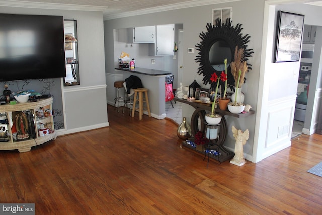 living room with visible vents, wood finished floors, baseboards, and ornamental molding