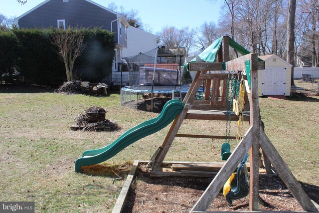 view of playground featuring a trampoline, a storage shed, a lawn, and an outdoor fire pit