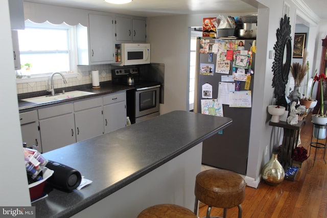 kitchen featuring a sink, dark countertops, wood finished floors, appliances with stainless steel finishes, and decorative backsplash