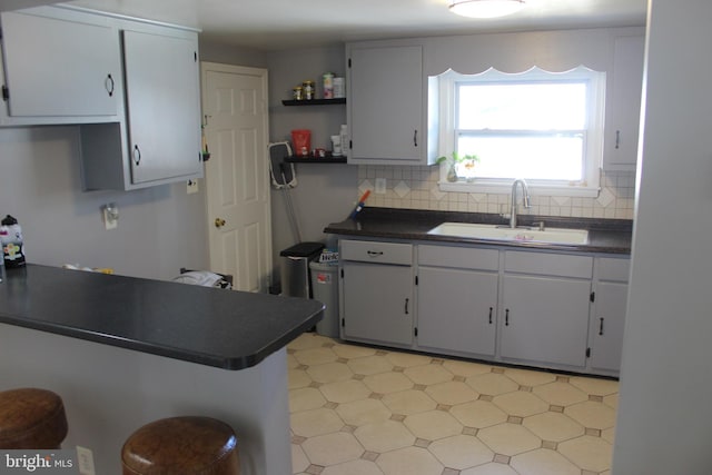 kitchen with dark countertops, tasteful backsplash, a sink, light floors, and open shelves