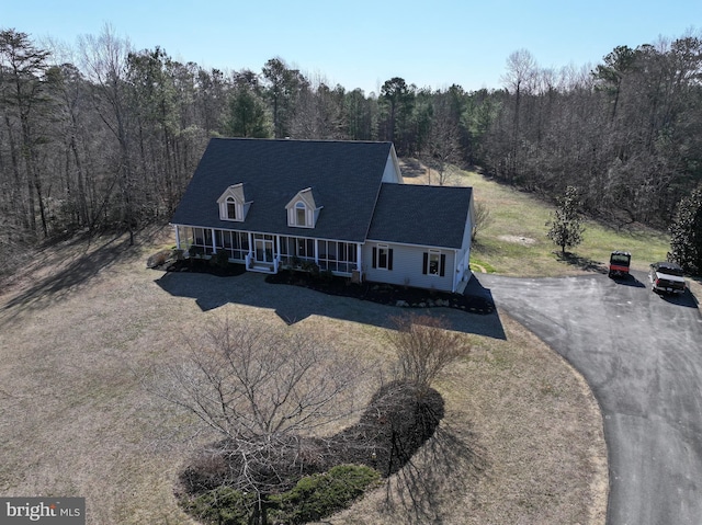 cape cod-style house with aphalt driveway, a porch, a shingled roof, and a view of trees