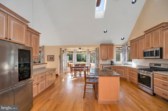 kitchen with appliances with stainless steel finishes, a breakfast bar, light wood-style floors, and high vaulted ceiling