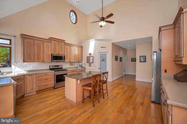 kitchen with a breakfast bar area, a kitchen island, a sink, appliances with stainless steel finishes, and light wood-type flooring