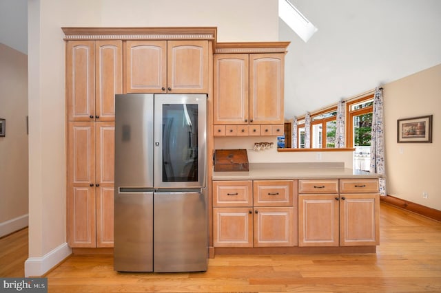 kitchen with baseboards, refrigerator with glass door, light countertops, light wood-style floors, and light brown cabinets