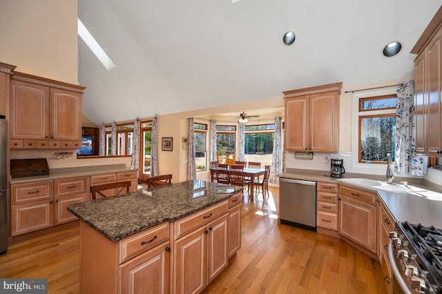 kitchen with light brown cabinets, stainless steel appliances, a sink, light wood-type flooring, and a center island