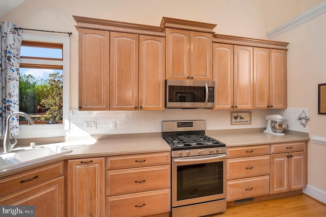 kitchen with tasteful backsplash, appliances with stainless steel finishes, light countertops, light wood-style floors, and a sink