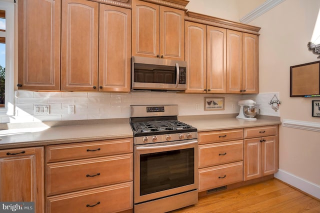 kitchen featuring stainless steel appliances, tasteful backsplash, light countertops, light wood-style floors, and light brown cabinets