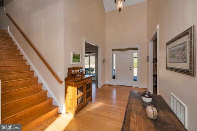 entrance foyer with baseboards, visible vents, a towering ceiling, stairs, and light wood-type flooring