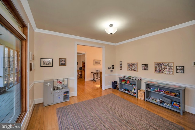 recreation room featuring baseboards, ornamental molding, and wood finished floors