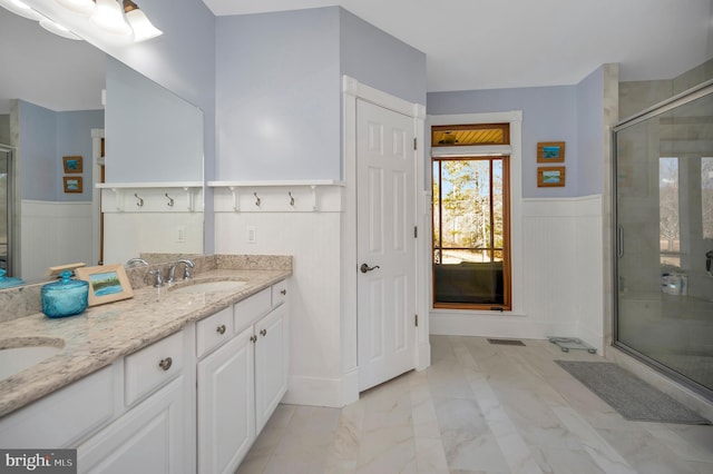 bathroom with double vanity, wainscoting, marble finish floor, a shower stall, and a sink