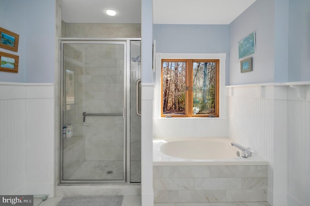 bathroom featuring a stall shower, a bath, and a wainscoted wall