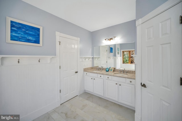 bathroom featuring marble finish floor, wainscoting, a sink, and double vanity