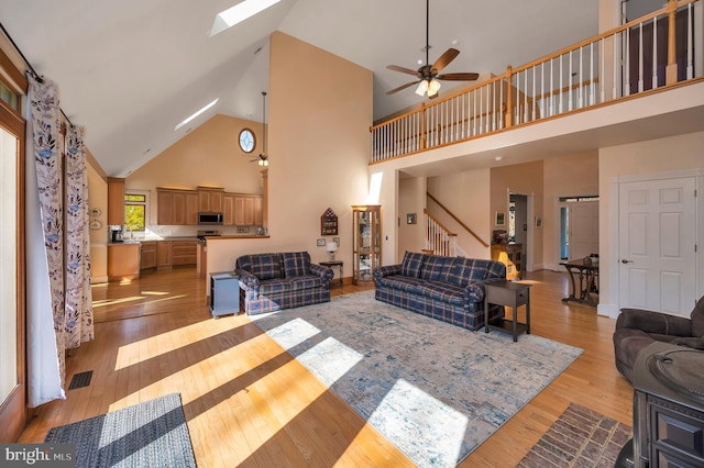 living area featuring a skylight, visible vents, light wood-style floors, a ceiling fan, and stairs