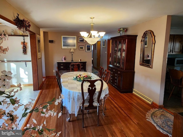 dining area with baseboards, a baseboard heating unit, a notable chandelier, and wood finished floors