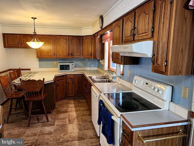 kitchen with under cabinet range hood, white appliances, brown cabinets, wallpapered walls, and pendant lighting