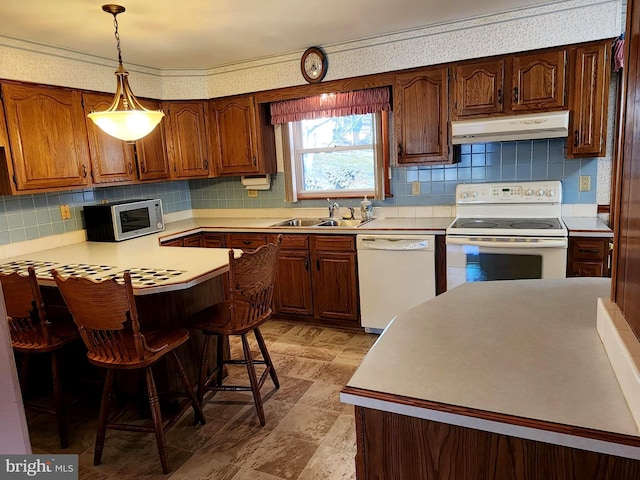 kitchen featuring light countertops, a sink, a peninsula, white appliances, and under cabinet range hood