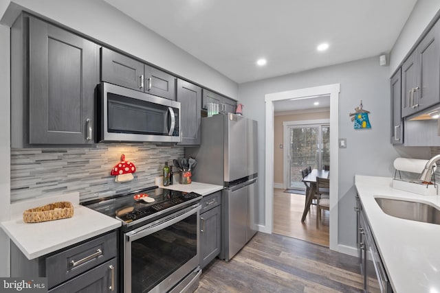 kitchen with appliances with stainless steel finishes, wood finished floors, a sink, light countertops, and backsplash