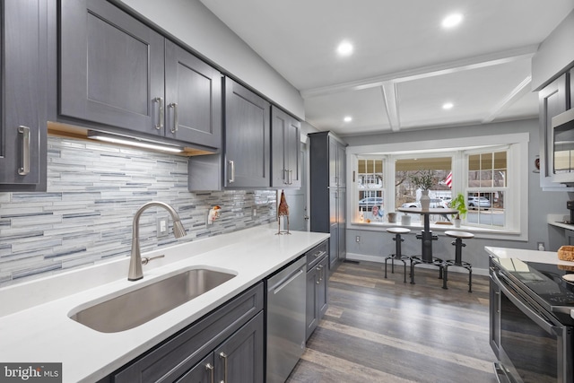 kitchen featuring dark wood finished floors, appliances with stainless steel finishes, a sink, light countertops, and backsplash