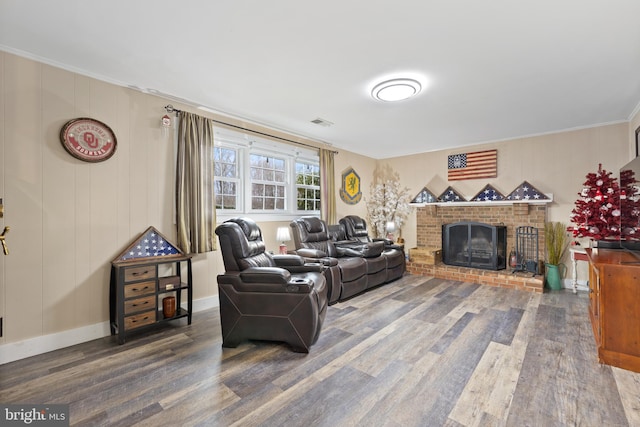 living room featuring wood finished floors, visible vents, baseboards, a brick fireplace, and crown molding