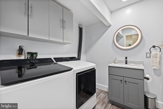 clothes washing area featuring light wood-style flooring, a sink, baseboards, cabinet space, and washer and clothes dryer