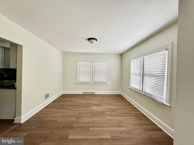 empty room with wood finished floors, visible vents, and baseboards