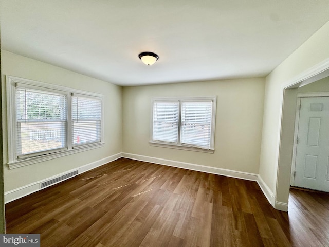 empty room with dark wood-style floors, visible vents, and baseboards