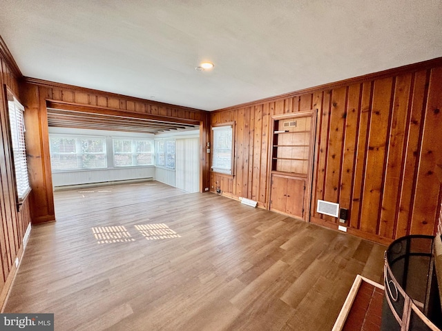 unfurnished living room with a wealth of natural light, visible vents, wood finished floors, and a baseboard heating unit